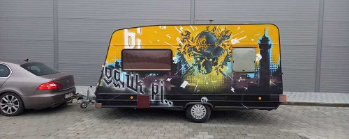 Obytný karavan s custom graffiti malbou, zobrazující energické motivy města Ostrava a rockovou hudbu. Design obsahuje siluety městského panoramatu a kytary v živých žlutých a černých barvách.